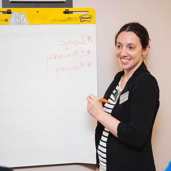 A women stands at a white flipchart holding a marker